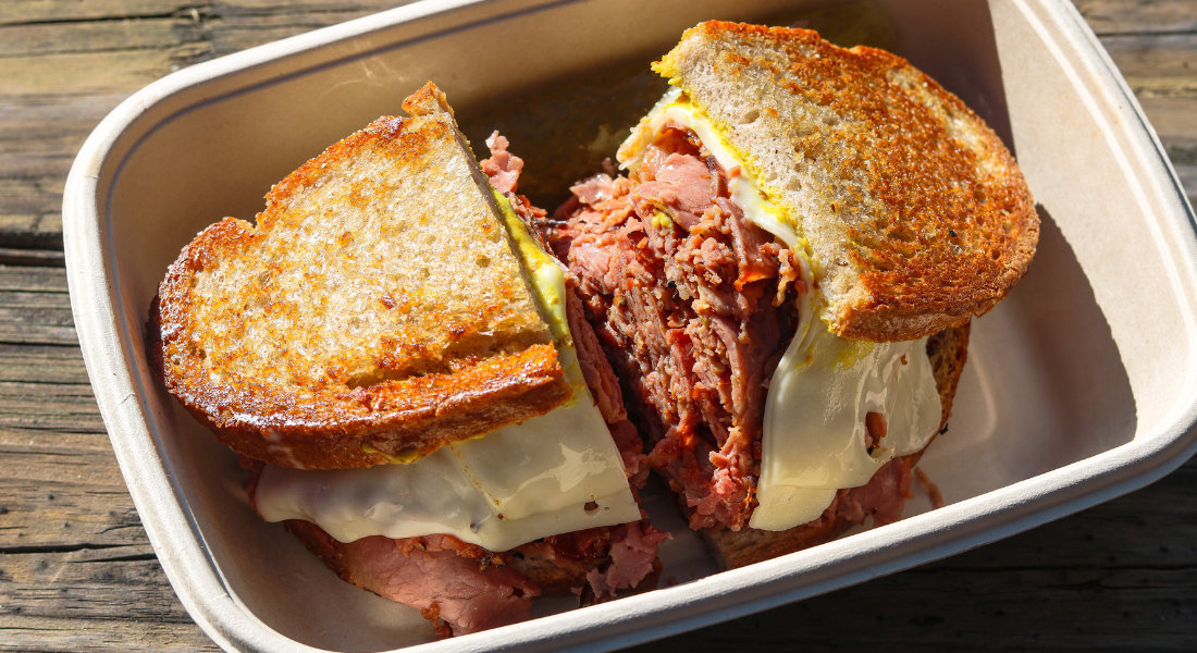Sandwich montréalais garni de viande fumée tranchée, de fromage fondu et servi avec des cornichons