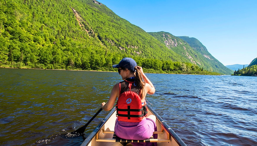 La rivière Malbaie Une femme vue de dos assise sur un canot, naviguant sur la rivière avec une vue sur les falaises