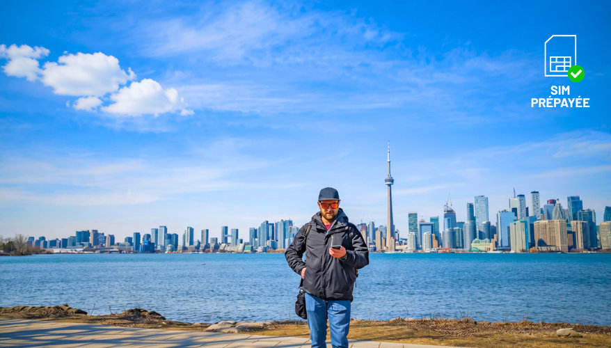 Sim locale un homme tenant son téléphone avec, dos à lui, la sky line sur la ville de Toronto
