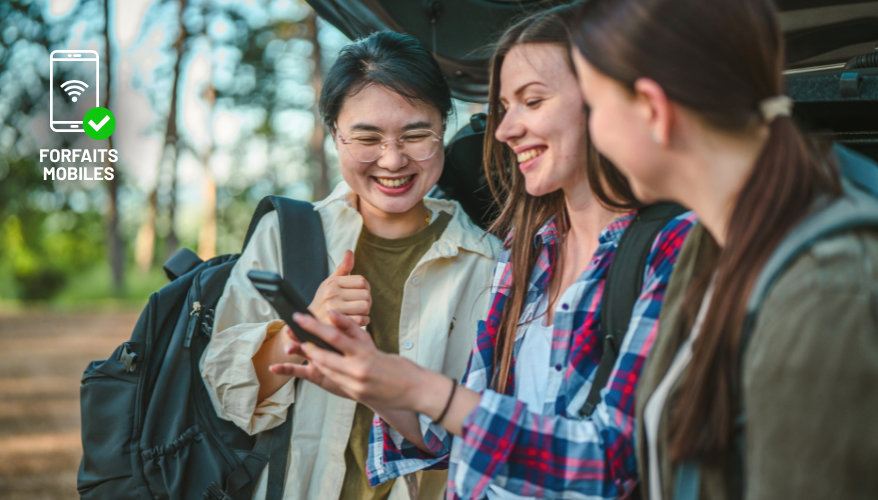 Forfait mobile 3 jeunes voyageuses regardent le téléphone d'une d'entre elles avec le sourire