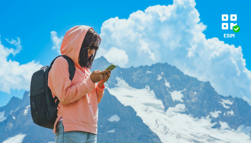 Une esim Une femme en montagne est sur son téléphone, elle peut facilement l'utiliser grâce a la eSIM