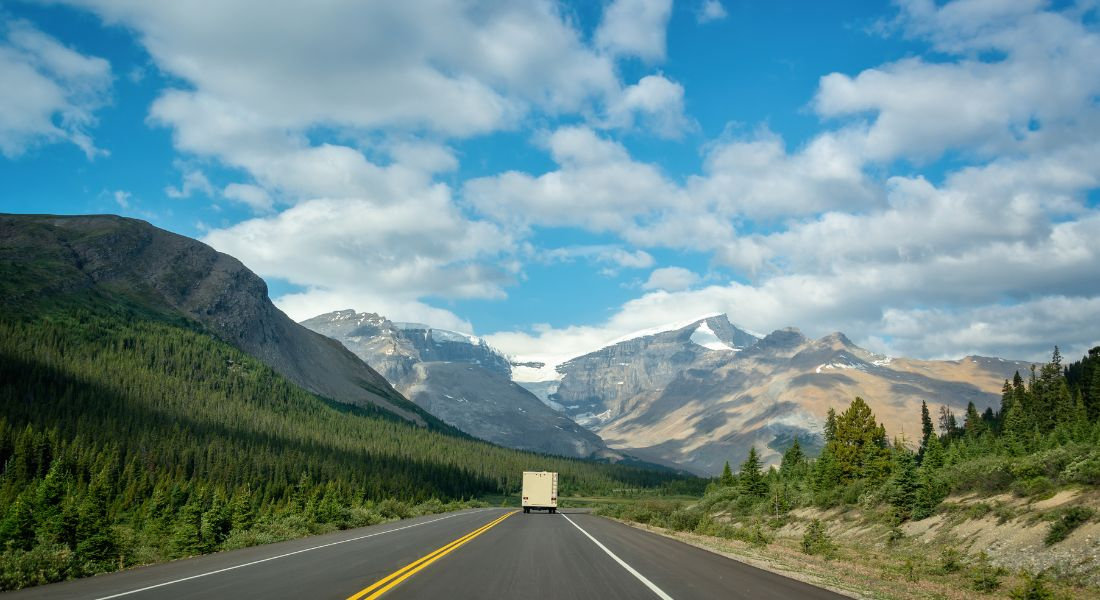Choose the right travel season RV on the road with the Rocky Mountains in the background