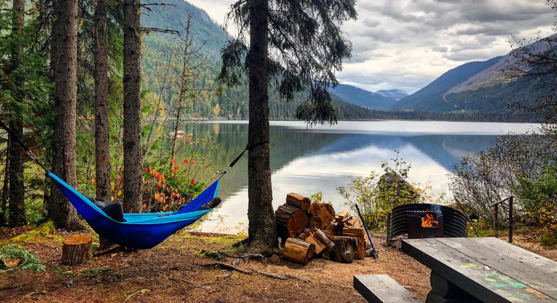 un emplacement de camping au bord d'un lac au canada avec un hamac feu de camp et table de pique-nique