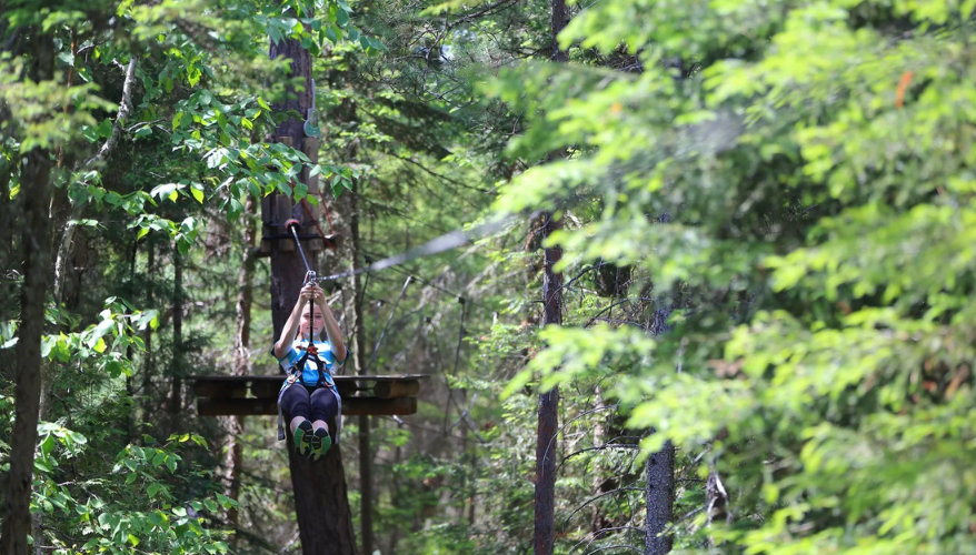 Adventure at Cap Jaseux A person zip-lining through the forest at Parc Aventures Cap Jaseux, Saguenay.