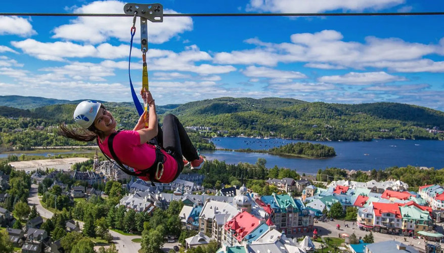 Zip-lining in Mont-Tremblant Person zip-lining over Mont-Tremblant village with views of the lake and mountains.
