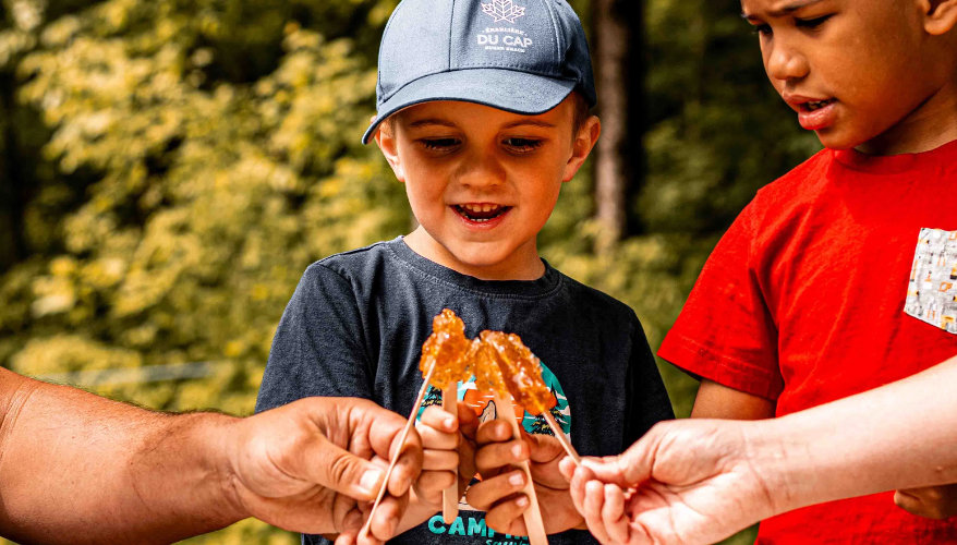 Experience a sugar shack in summer Children enjoying maple taffy on snow during a sugar shack experience in Quebec.