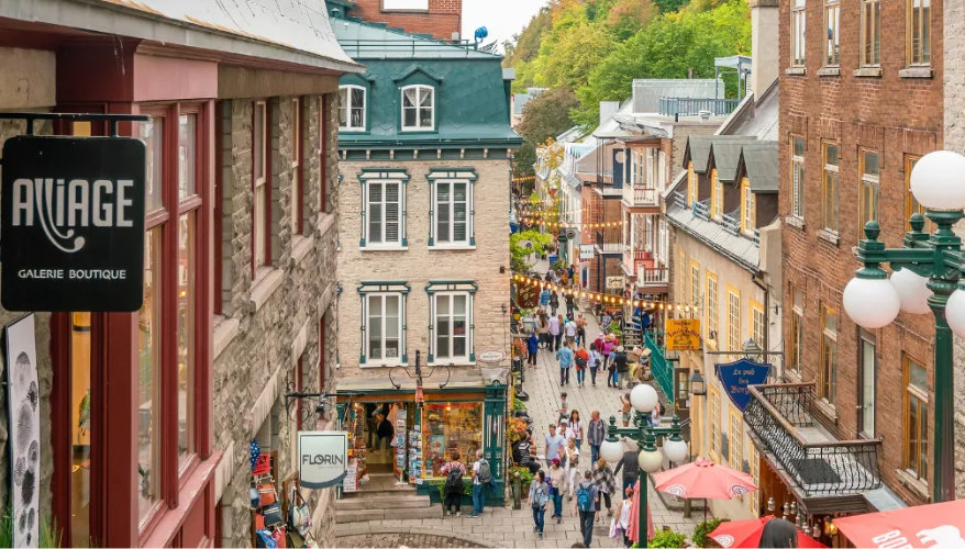 Visiter le Vieux-Québec à pied Rue animée du Vieux-Québec bordée de bâtiments historiques, de boutiques et de terrasses.