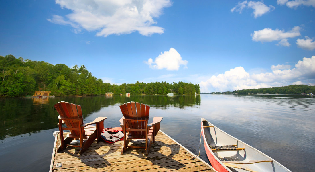 Deux chaises Adirondacks au bord d'un lac avec un canot 