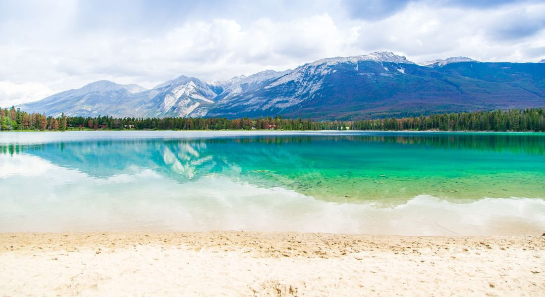 Plage de sable blanc au bord du Lac Edith avec les montagnes enneigées en arrière-plan