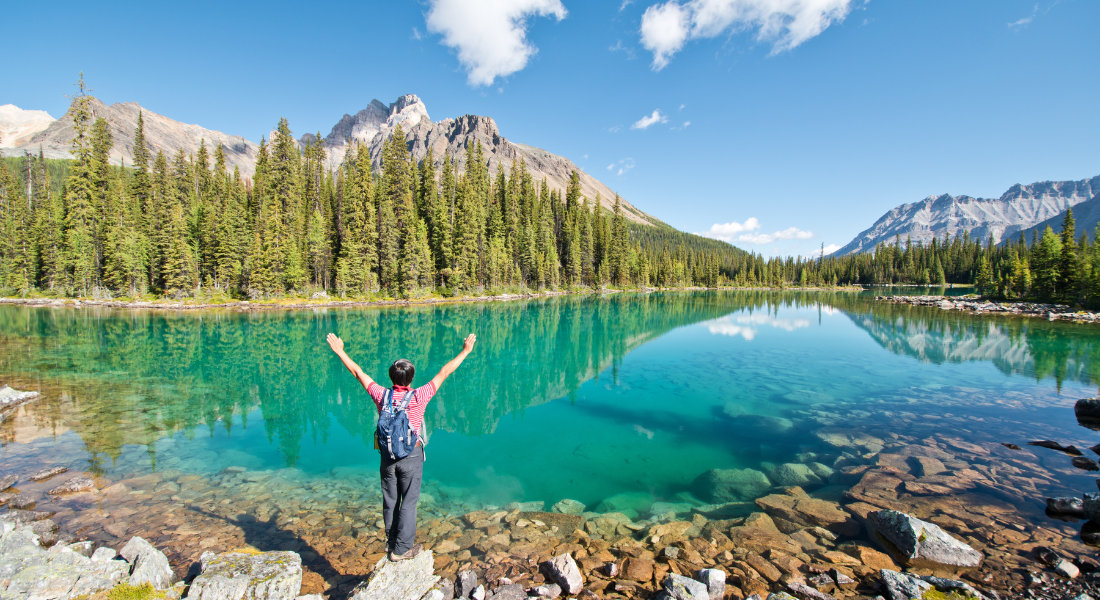 personne les bras en l'air devant un lac bleu turquoise dans le parc national de Yoho