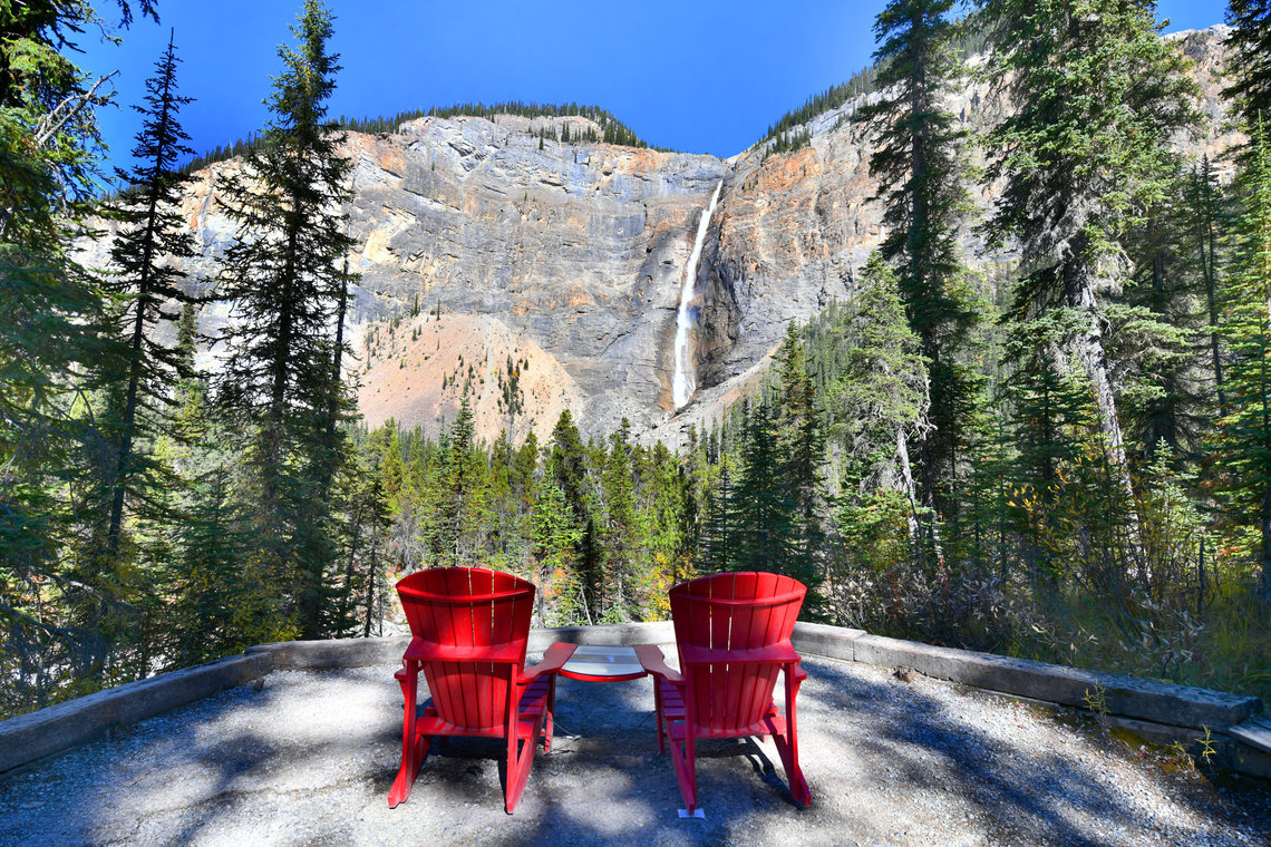 Red chairs facing Takakkaw Falls, one of the highest waterfalls in the Canadian Rockies.