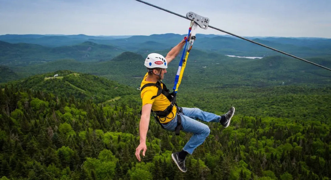 Zip line at Mont Tremblant Man descending by zip line over a forest