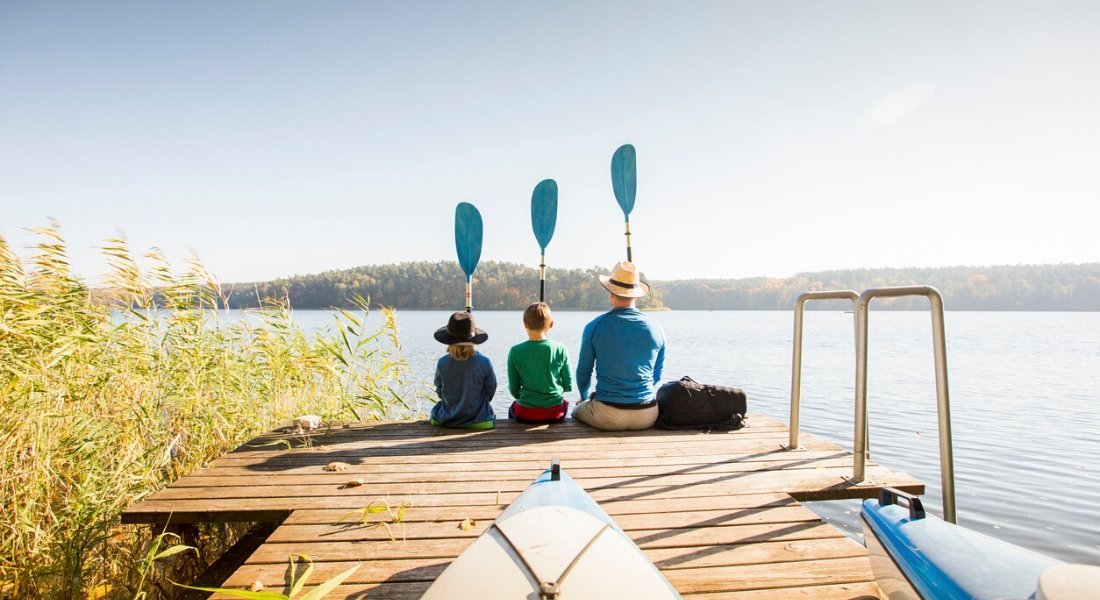 Père et ses deux enfants assis sur le ponton d'un lac avec une pagaie dans la main