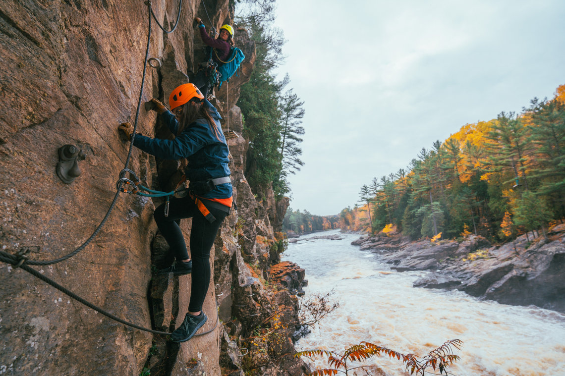 Via ferrata in Quebec at fall Two people doing a via ferrata above a river in autumn in Quebec