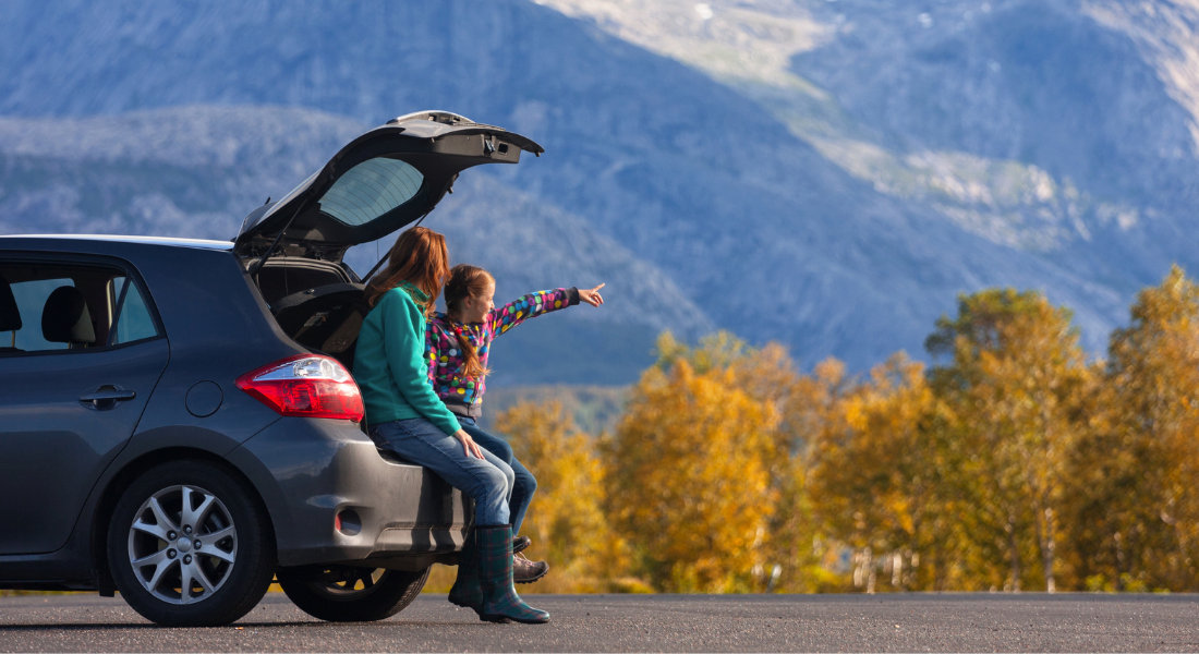 une mère et sa fille qui admirent le paysage en étant assise sur le bord du coffre de la voiture