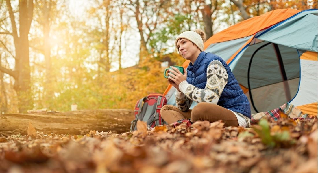Camping à l'automne au Québec Jeune femme buvant un café assise par terre devant sa tente en automne