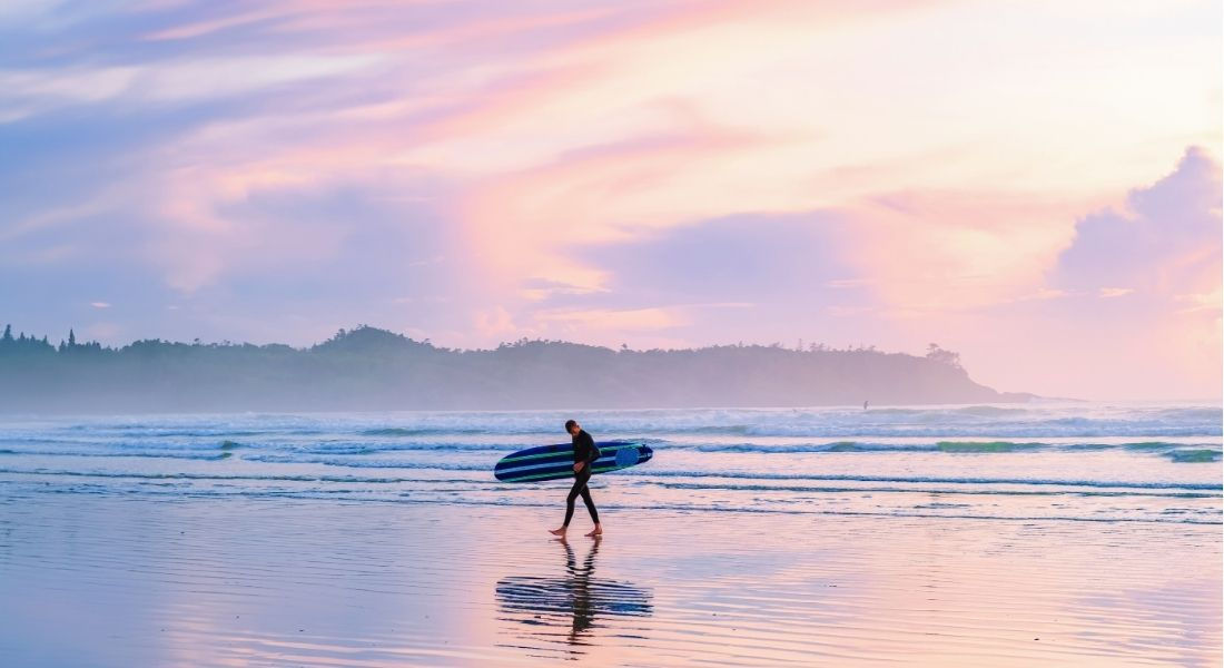 Surfeur marchant sur la plage avec sa planche sous le bras au coucher du soleil Surf île de vancouver