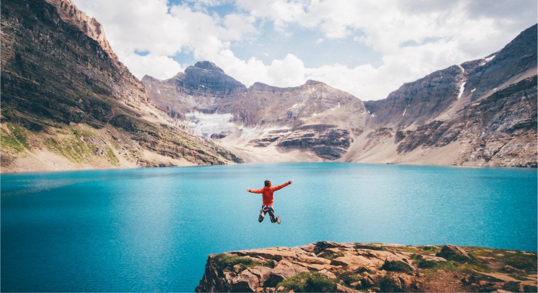 Homme saute de joie devant un lac de l'ouest du Canada