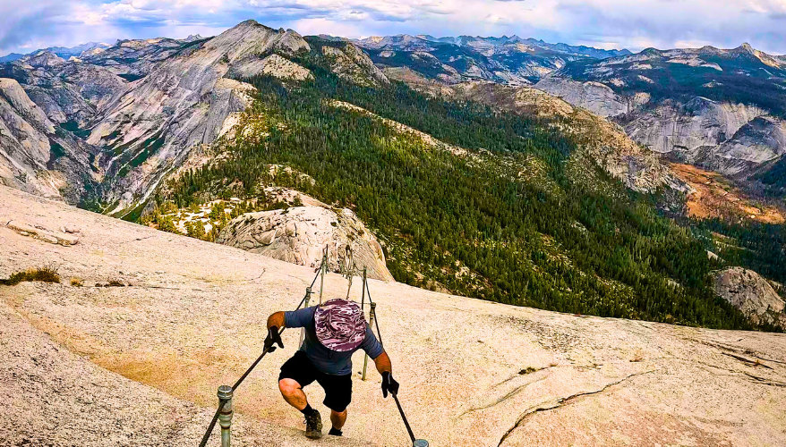 Half Dome A man climbing the north face of Half Dome, holding onto cables fixed in the rock.