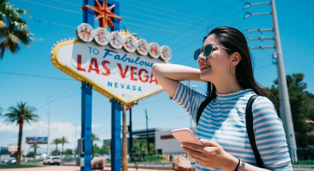 A young woman in front of the “Welcome to Fabulous Las Vegas” sign using her phone to stay connected while travelling.