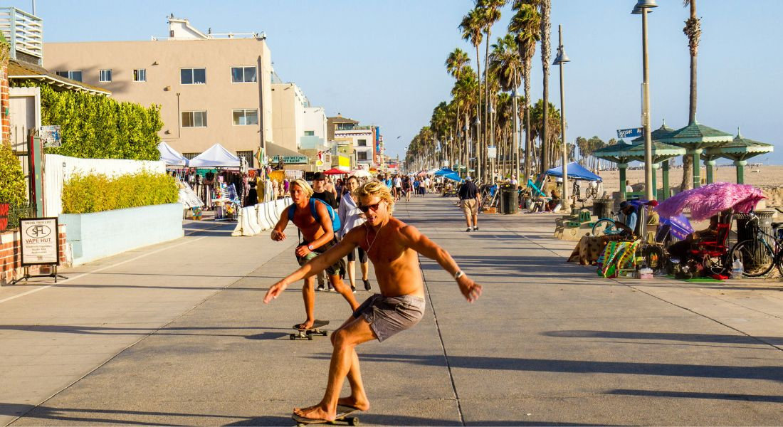 Vacation vibes along Venice Beach Skaters rolling along the beach under the palm trees of Venice Beach